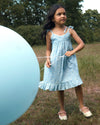 Early Sunday, Alena dress in Tonal Floral Blue color, made from printed cotton tiny swiss dobby fabric, featuring tie-up shoulder straps, gathered flare, and ruffled hem, shown in a front view of model wearing.