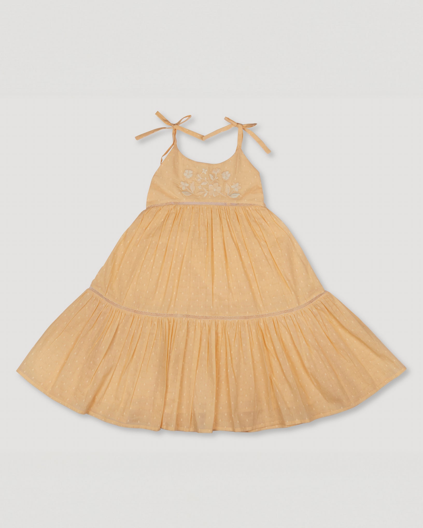 Early Sunday, Alice Dress in Vanilla color, made from Cotton Dobby Swiss Dots fabric, featuring sleeveless with adjustable tie-up straps and a tiered silhouette, shown in a front flat-lay view