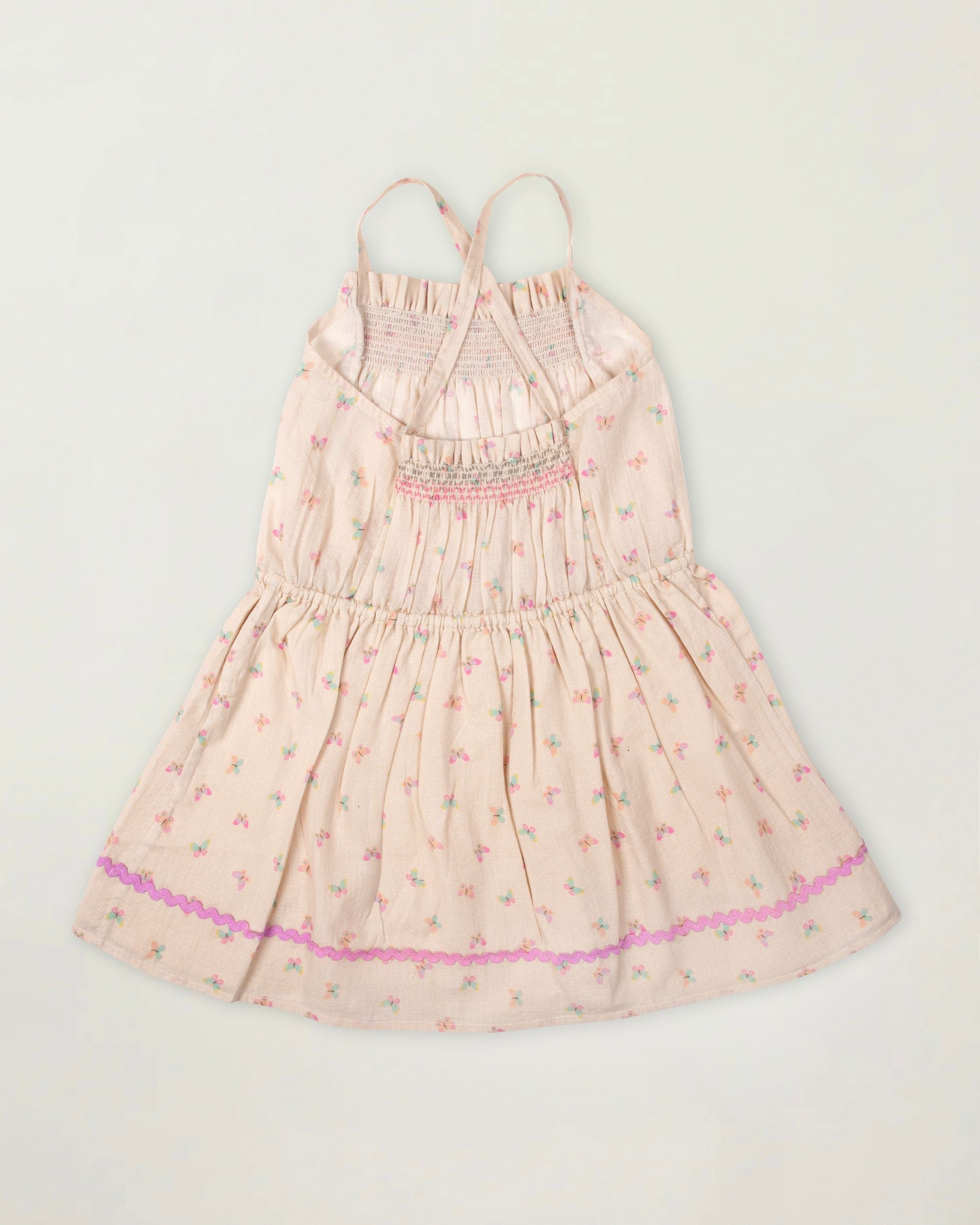 Early Sunday, Alisson Dress in butterfly print color, made from printed cotton tiny swiss dobby fabric, featuring smocked bodice, adjustable shoulder straps, sweet tassel accents, and a flowy gathered skirt, shown in a back flat-lay view.