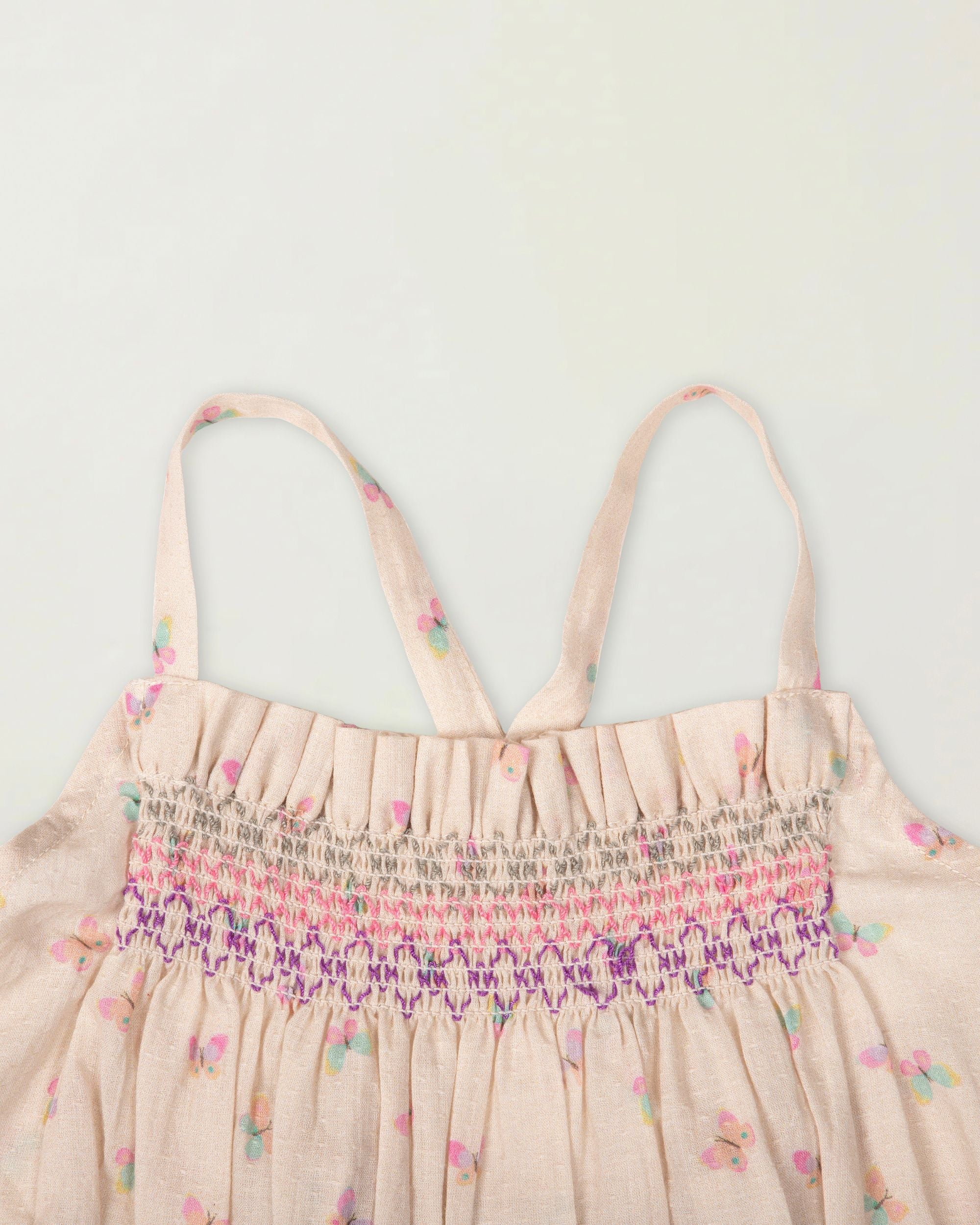 Early Sunday, Alisson Dress in butterfly print color, made from printed cotton tiny swiss dobby fabric, featuring smocked bodice, adjustable shoulder straps, sweet tassel accents, and a flowy gathered skirt, shown in a closeup flat-lay view.