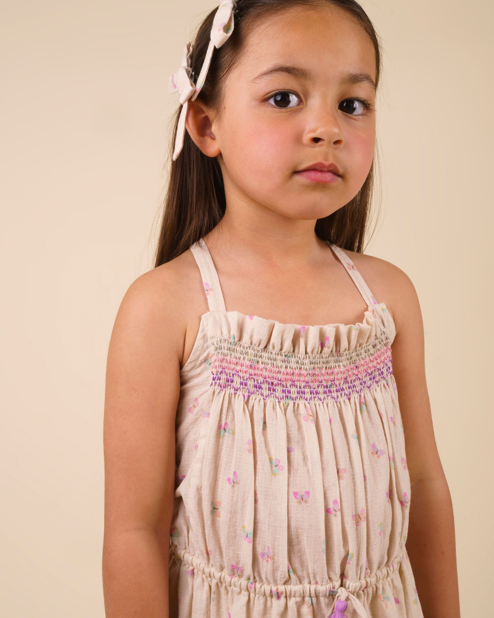 Early Sunday, Alisson Dress in butterfly print color, made from printed cotton tiny swiss dobby fabric, featuring smocked bodice, adjustable shoulder straps, sweet tassel accents, and a flowy gathered skirt, shown in a front view of model wearing.