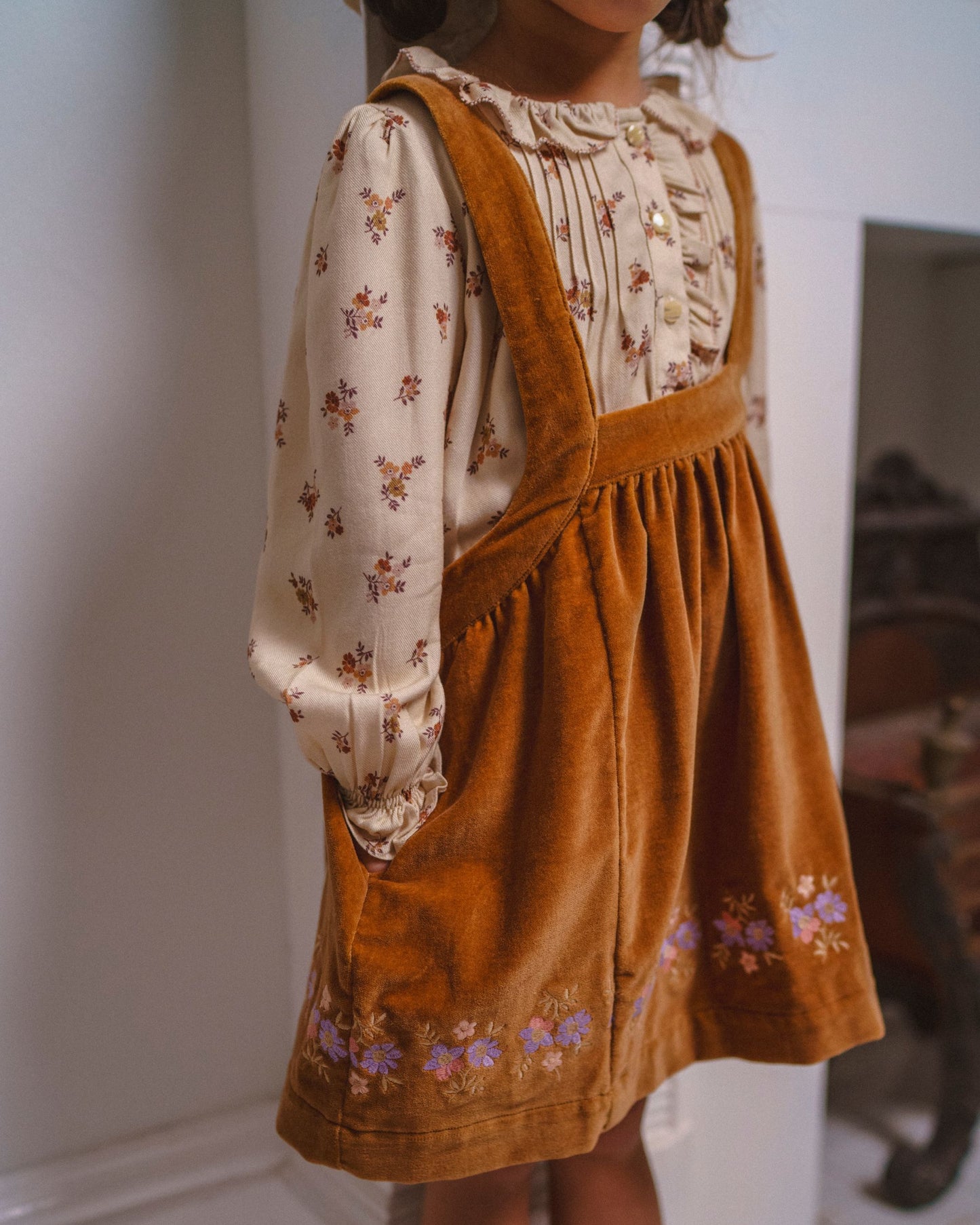 Early Sunday, Anni Skirt in Almond, made from Dyed Cotton Velvet fabric, featuring Delicate floral embroidery along the hem with playful cross-back straps, shown in a close-up shot of a model wearing it during a studio shoot