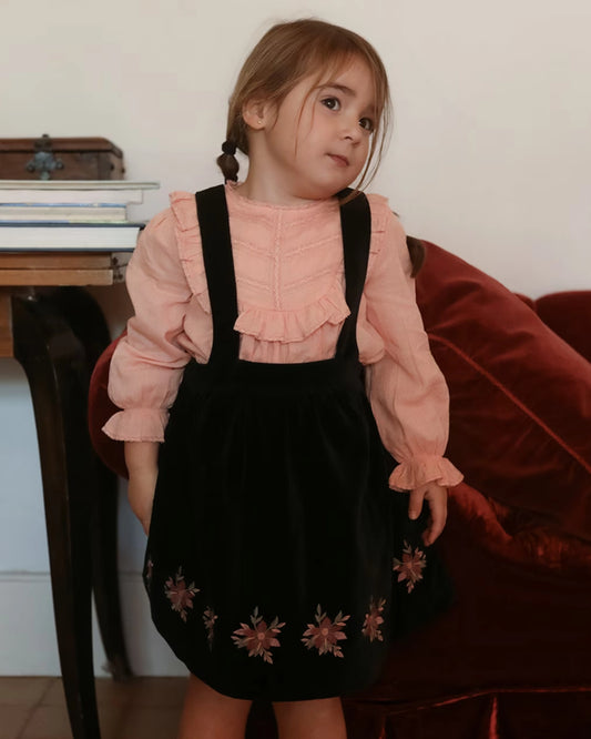 Early Sunday, Annie Skirt in Black, made from Cotton Velvet Velour's fabric, featuring an A-line silhouette with adjustable cross-back straps and soft gathers, shown in a front view of model wearing it