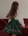 Early Sunday, Annie Skirt in Forest Green, made from Cotton Velvet Velour's fabric, featuring an A-line silhouette with adjustable cross-back straps and soft gathers, shown in a side view of model wearing it