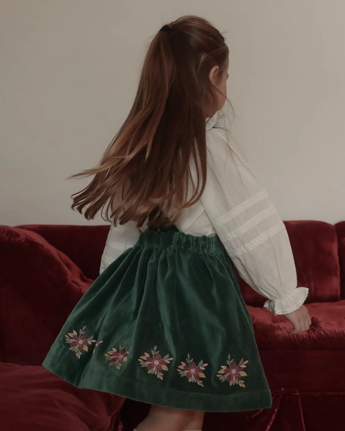 Early Sunday, Annie Skirt in Forest Green, made from Cotton Velvet Velour's fabric, featuring an A-line silhouette with adjustable cross-back straps and soft gathers, shown in a side view of model wearing it