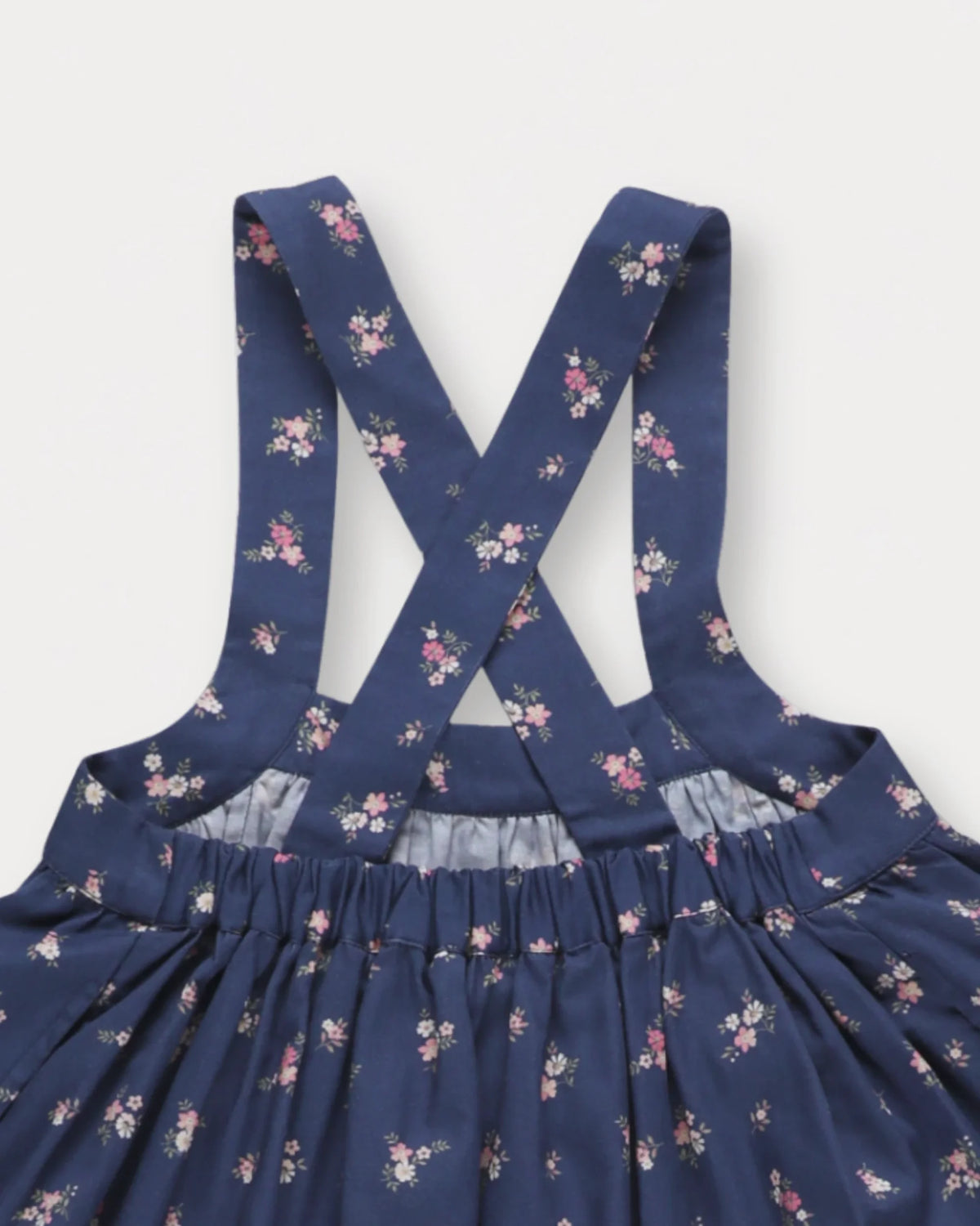 Early Sunday, Annie Skirt in Ditsy Bouquet Navy, made from Printed Cotton Satin fabric, featuring an A-line silhouette with adjustable cross-back straps and soft gathers, shown in a closeup flat-lay view