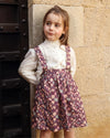 Early Sunday, Annie Skirt in Garden Flowers Plum, made from Printed Cotton Satin fabric, featuring an A-line silhouette with adjustable cross-back straps and soft gathers, shown in a front view of model wearing outdoors