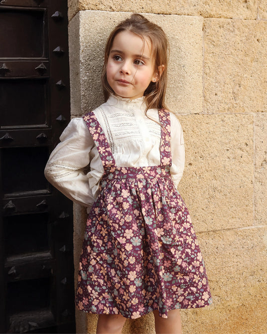 Early Sunday, Annie Skirt in Garden Flowers Plum, made from Printed Cotton Satin fabric, featuring an A-line silhouette with adjustable cross-back straps and soft gathers, shown in a front view of model wearing outdoors