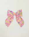 Early Sunday, Audrey Clip in Emma Floral Purple color, made from Organic Printed Cotton Cambric fabric, featuring a fabric bow design with a secure hair clip fastening, shown in a front flat-lay view