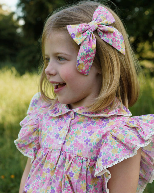 Early Sunday, Audrey Clip in Emma Floral Purple color, made from Organic Printed Cotton Cambric fabric, featuring a fabric bow design with a secure hair clip fastening, shown in a side view of model wearing it