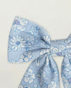 Early Sunday, Audrey Clip in Tonal Floral Blue color, made from Printed 70% Cotton, 30% Linen fabric, featuring a fabric bow design with a secure hair clip fastening, shown in a closeup flat-lay view