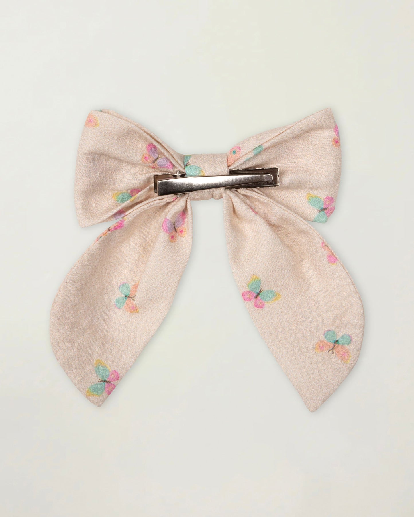 Early Sunday, Audrey Clip in Butterflies print, made from Printed Cotton Tiny Swiss Dobby fabric, featuring a fabric bow design with a secure hair clip fastening, shown in a back flat-lay view
