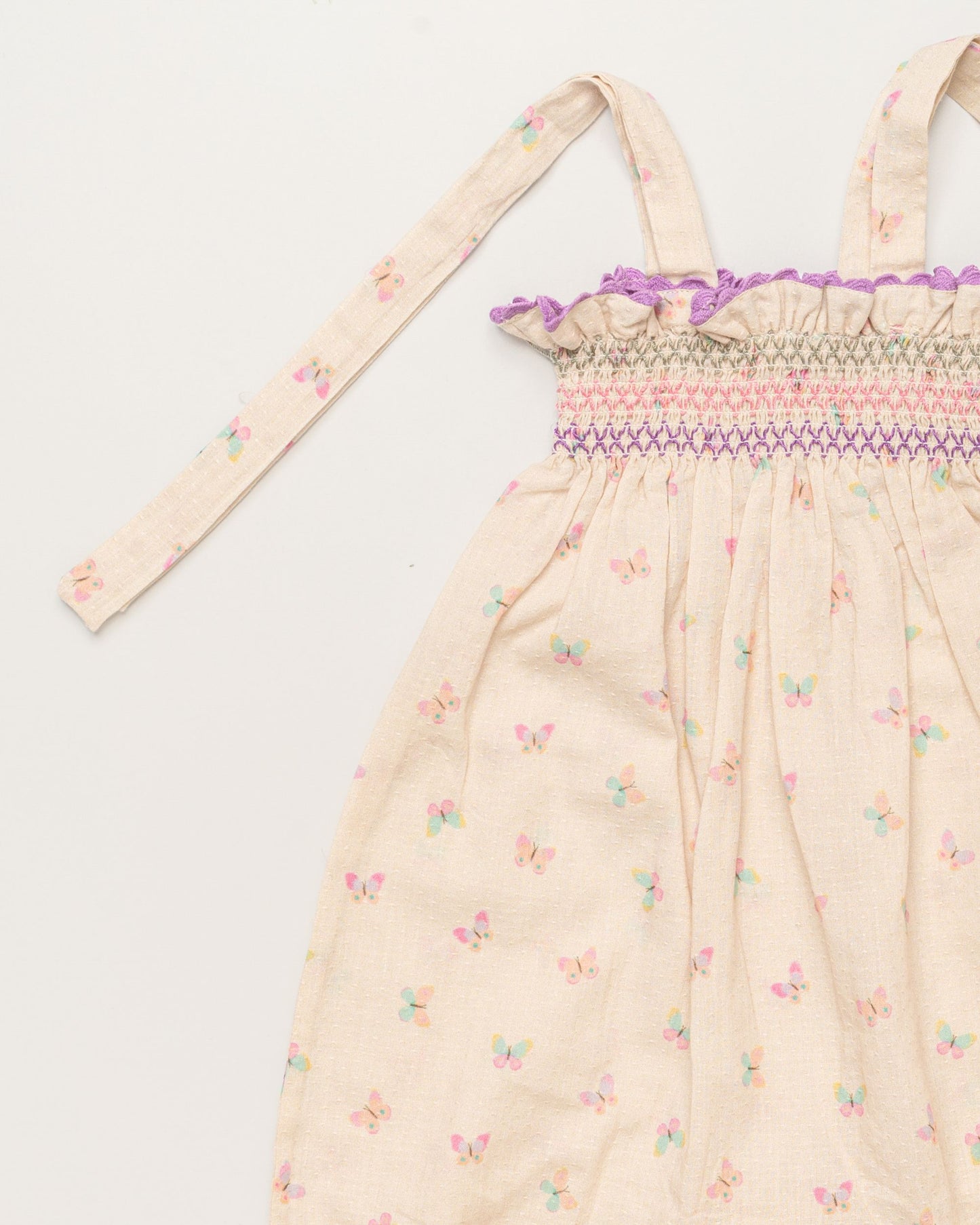 Early Sunday, Audrey Overall Baby Romper in Butterflies print, made from 100% Cotton Swiss Dobby Tiny Dots fabric, featuring tie-up shoulder straps with dot texture & smocked waistband, shown in a closeup flat-lay view