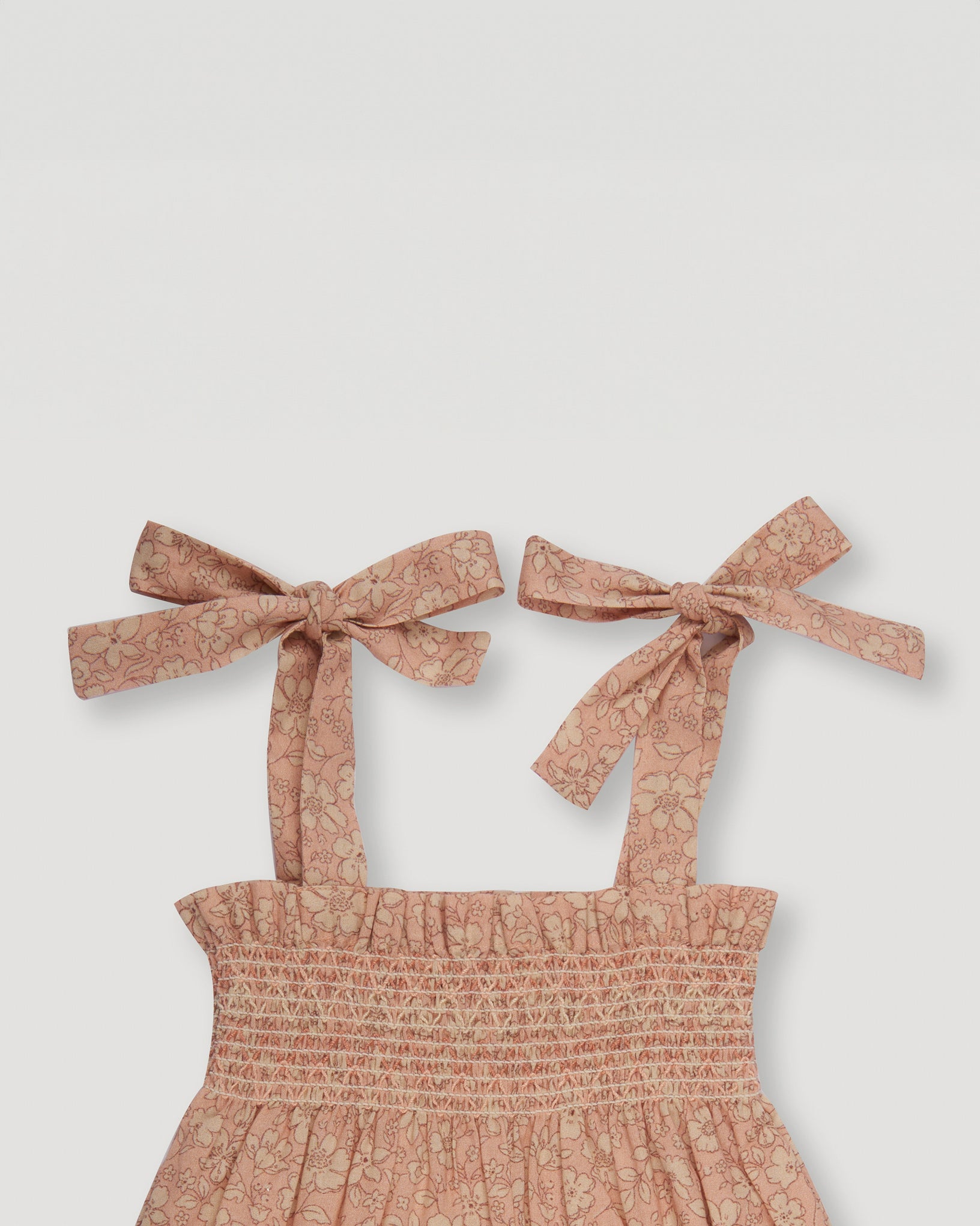 Early Sunday, Audrey Smocked Romper in Garden Flowers print, made from Printed Cotton Cambric fabric, featuring smocked chest and tie up straps, shown in a close up flat-lay view