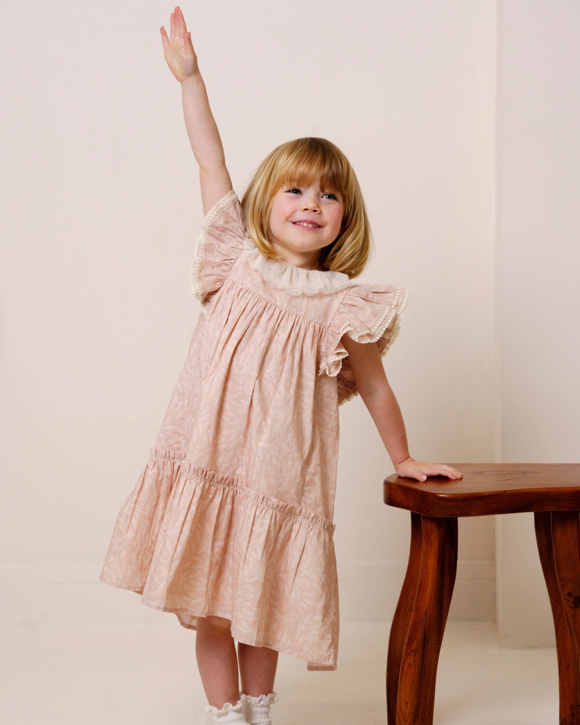 Early Sunday, Aurelia Dress in Feather print, made from Printed Cotton Cambric fabric, featuring Layered ruffles with flutter sleeves, shown in a front view of model wearing it
