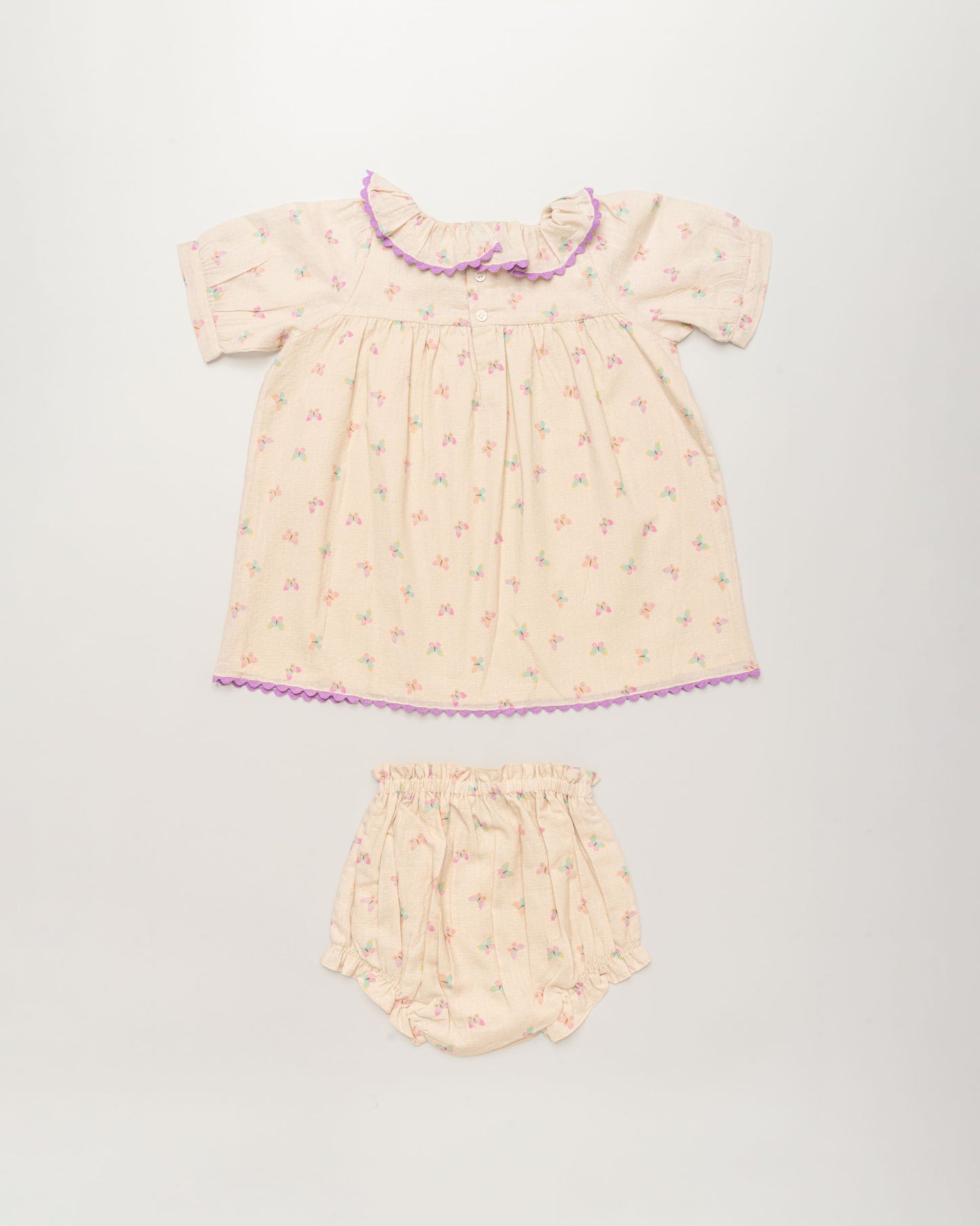 Early Sunday, Baby Bella Dress with Bloomer in Butterflies print, made from 100% Cotton Swiss Dobby Tiny Dots fabric, featuring short puff sleeves with a lilac lace & matching bloomers, shown in a back flat-lay view