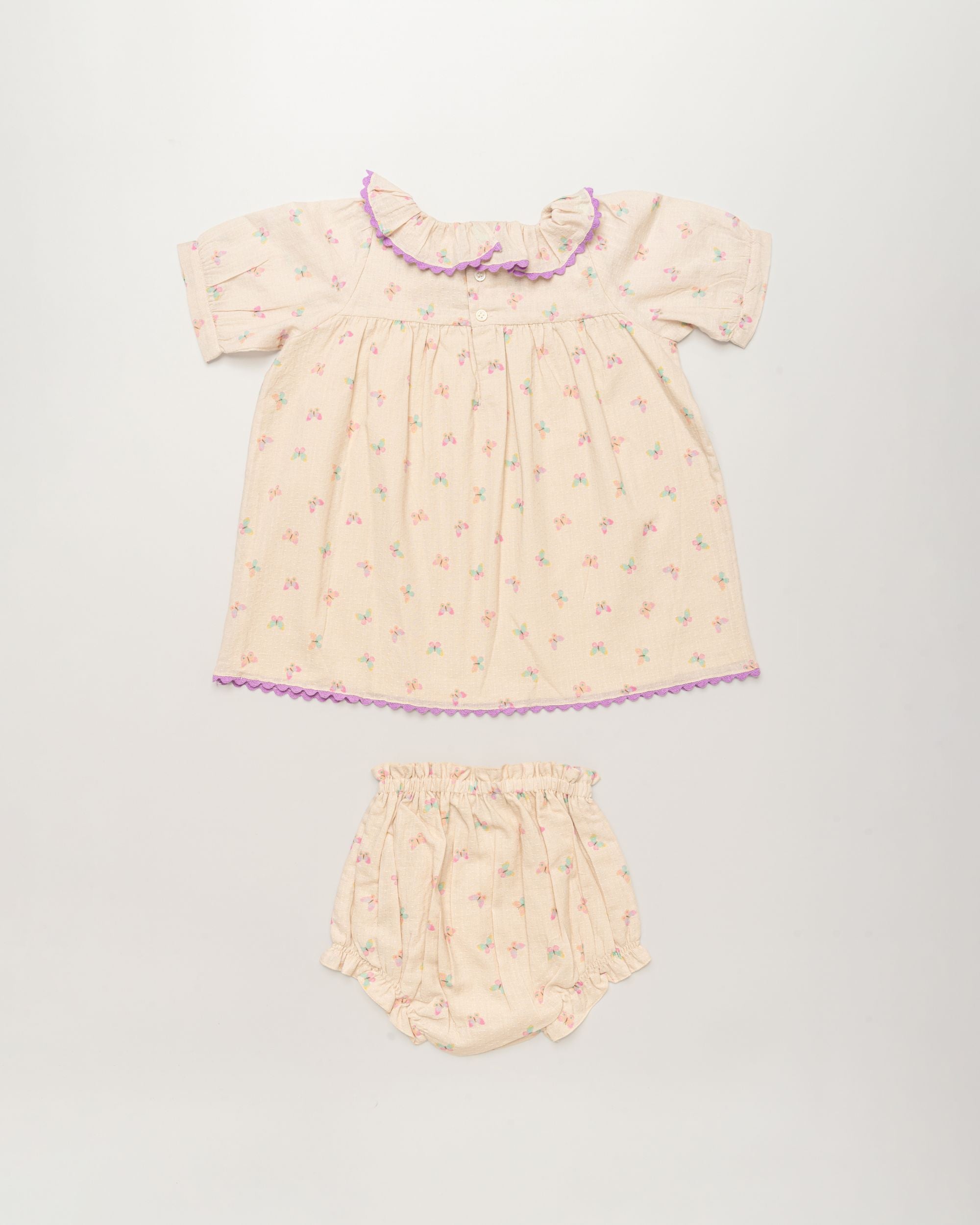 Early Sunday, Baby Bella Dress with Bloomer in Butterflies print, made from 100% Cotton Swiss Dobby Tiny Dots fabric, featuring short puff sleeves with a lilac lace & matching bloomers, shown in a back flat-lay view