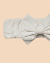 Early Sunday, Baby's Bow Headband in Ivory color, made from All-Over Embroidered Fabric fabric, featuring a wide bow design, shown in a closeup flat-lay view