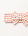 Early Sunday, Baby's Bow Headband in Peony color, made from Gingham Check fabric, featuring a wide bow design, shown in a closeup flat-lay view