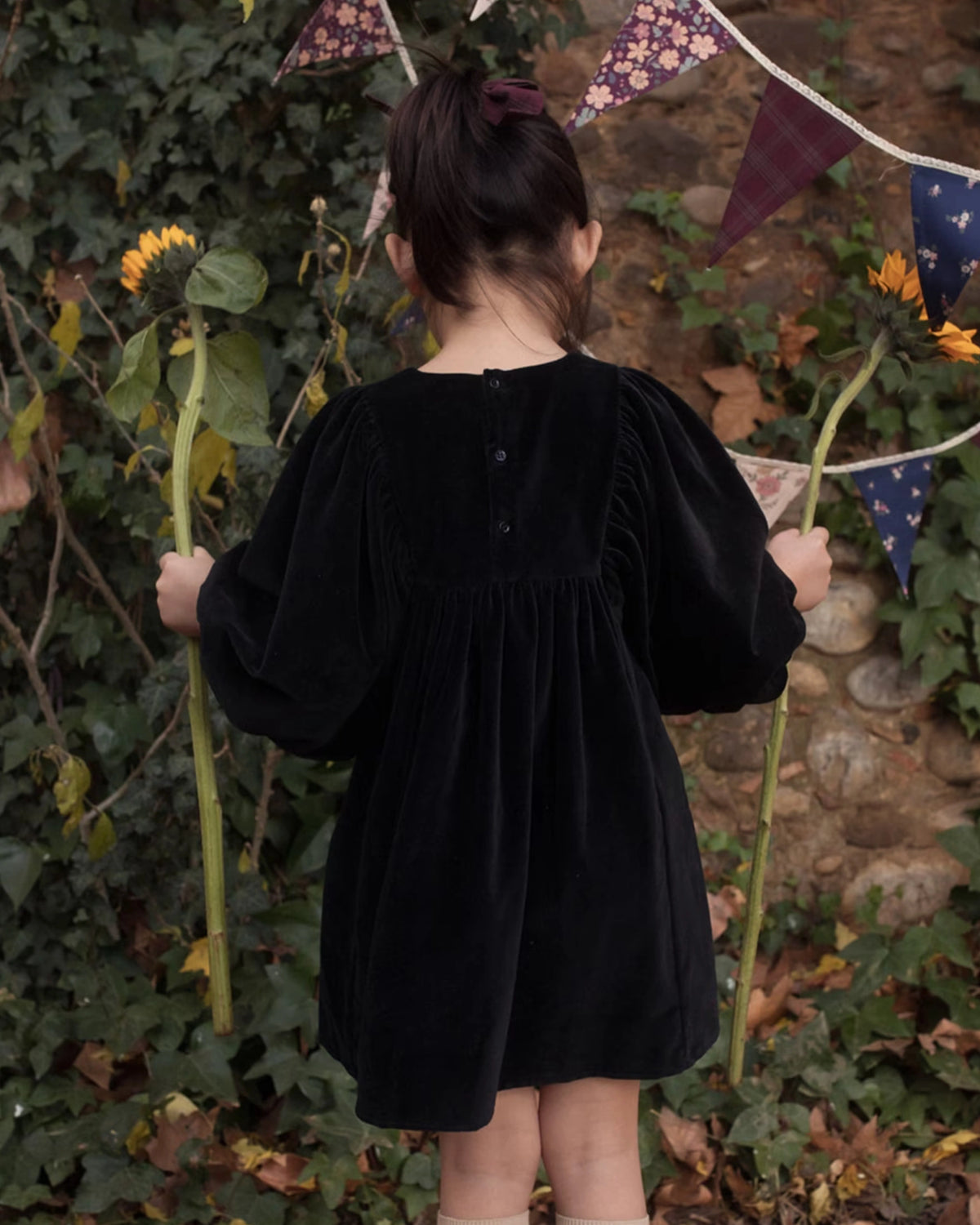Early Sunday, Belle Dress in Black, made from Cotton Velvet Velour's fabric, featuring a flowing silhouette with puff sleeves and gentle gathers, shown in a back view of model wearing outdoors