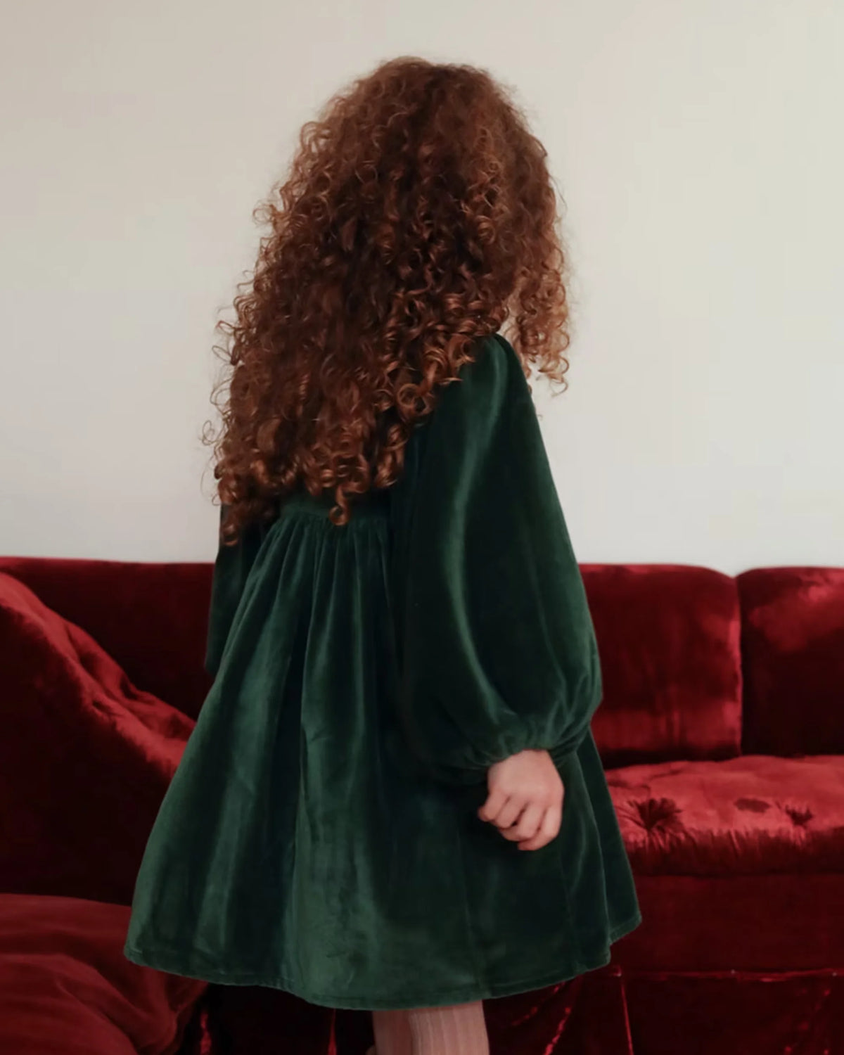 Early Sunday, Belle Dress in Forest Green, made from Cotton Velvet Velour's fabric, featuring a flowing silhouette with puff sleeves and gentle gathers, shown in a back view of model wearing it