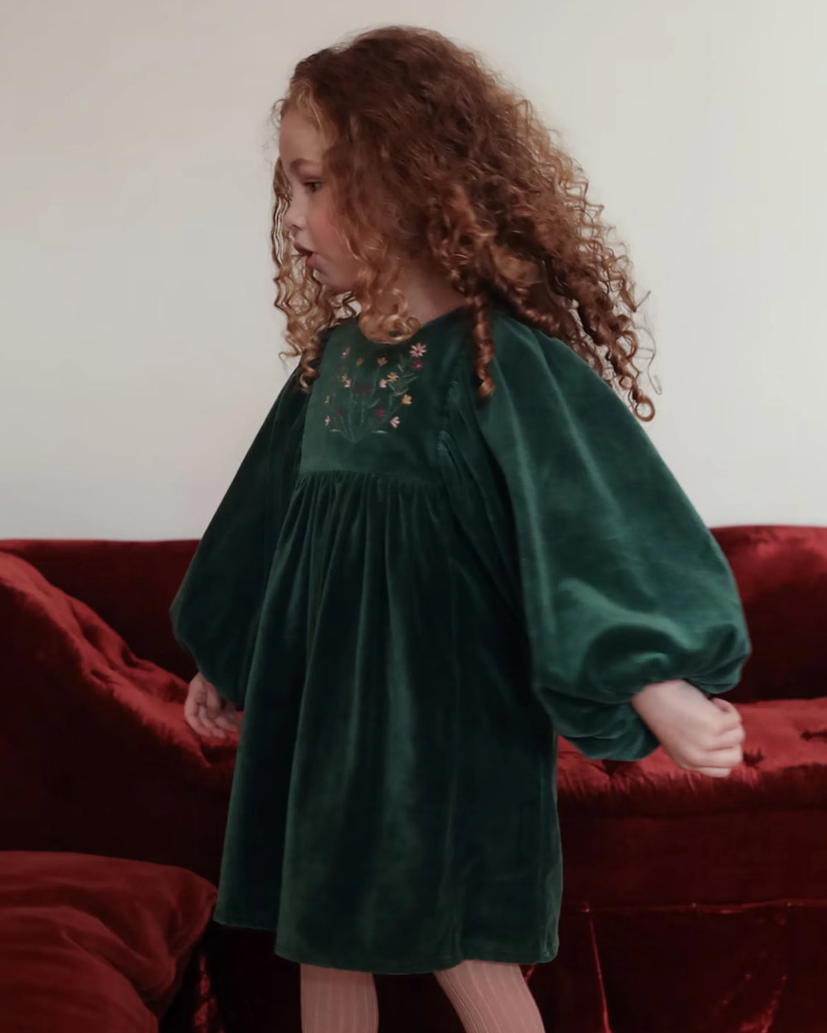 Early Sunday, Belle Dress in Forest Green, made from Cotton Velvet Velour's fabric, featuring a flowing silhouette with puff sleeves and gentle gathers, shown in a side view of model wearing it
