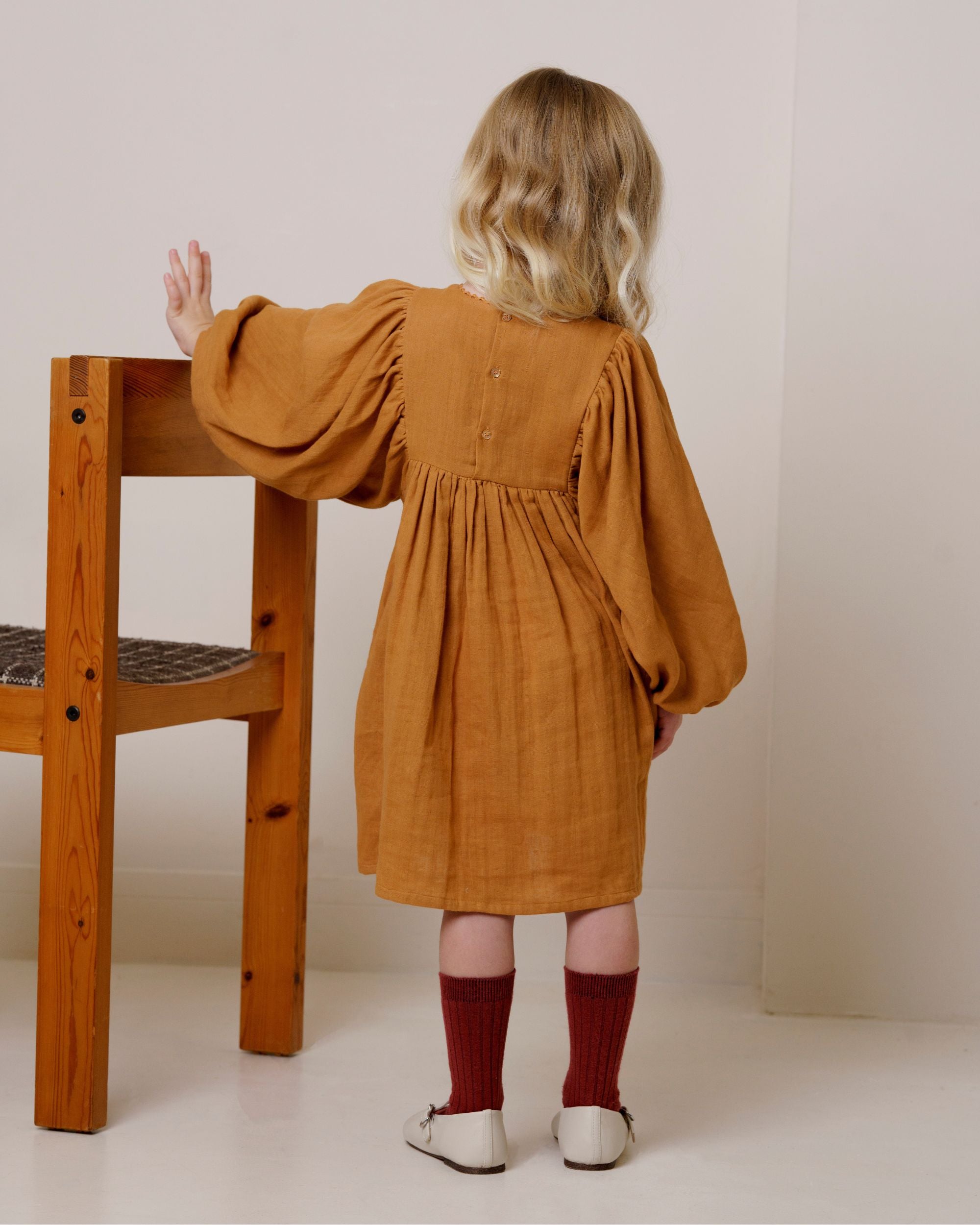 Early Sunday, Belle Dress in Almond, made from Dyed Cotton Double Gauze fabric, featuring Hand-embroidered floral bodice with voluminous puff sleeves for a soft, enchanting silhouette, shown in a back view of model wearing it