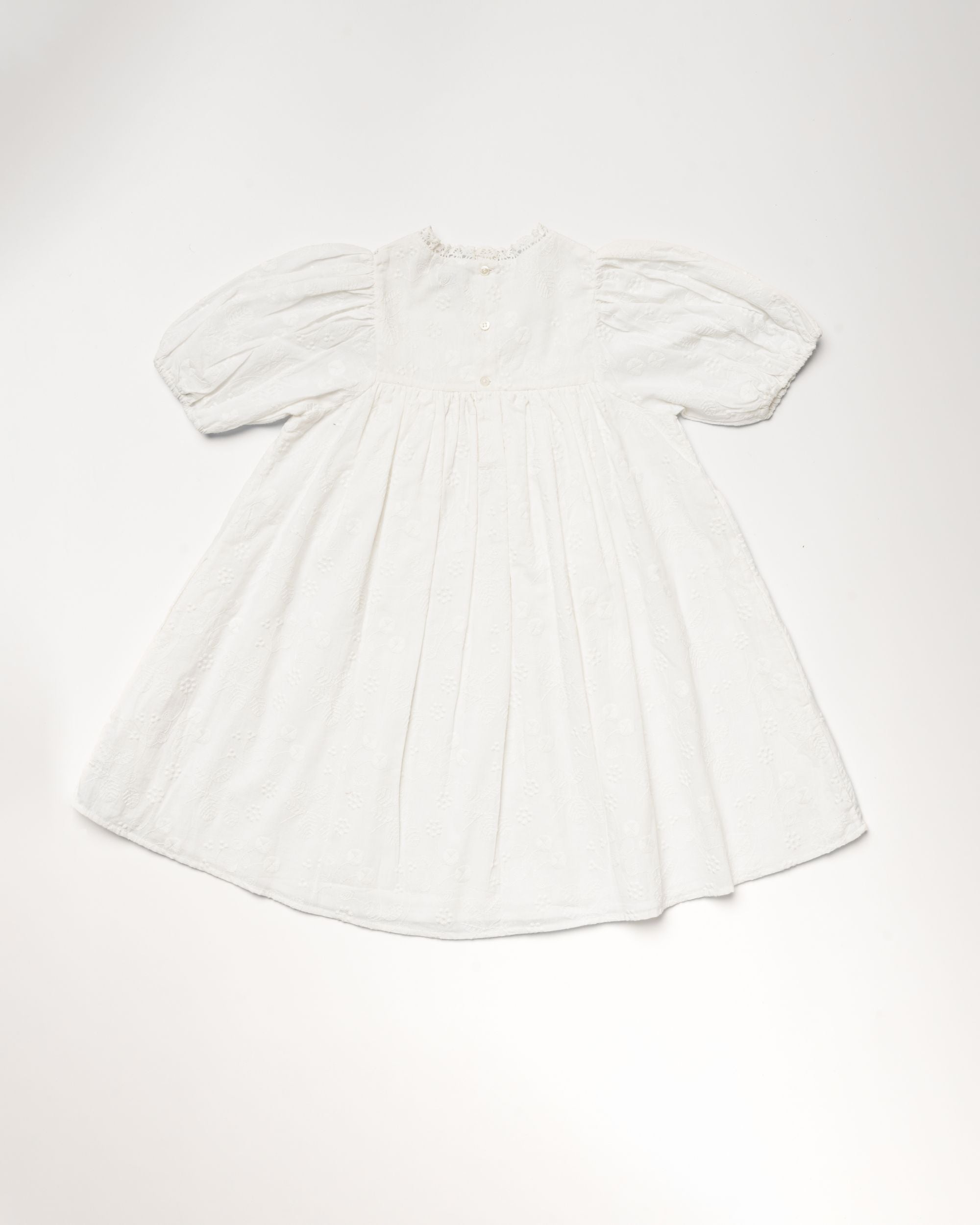 Early Sunday, Beth Dress in Ivory color, made from 100% cotton all over embroidered fabric, featuring Puff sleeves, contrast scalloped collar for a vintage touch, shown in a back flat-lay view.