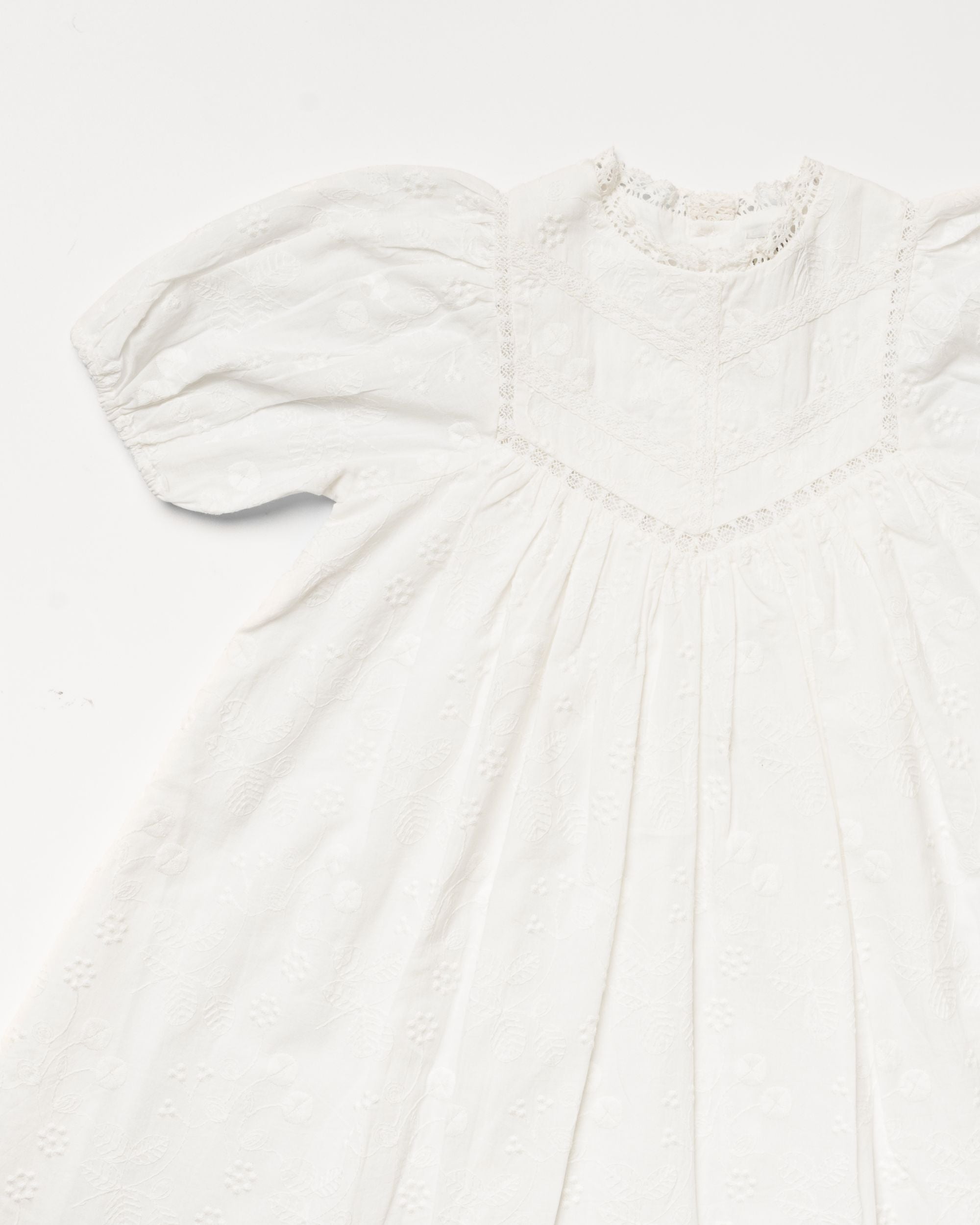 Early Sunday, Beth Dress in Ivory color, made from 100% cotton all over embroidered fabric, featuring Puff sleeves, contrast scalloped collar for a vintage touch, shown in a closeup flat-lay view.
