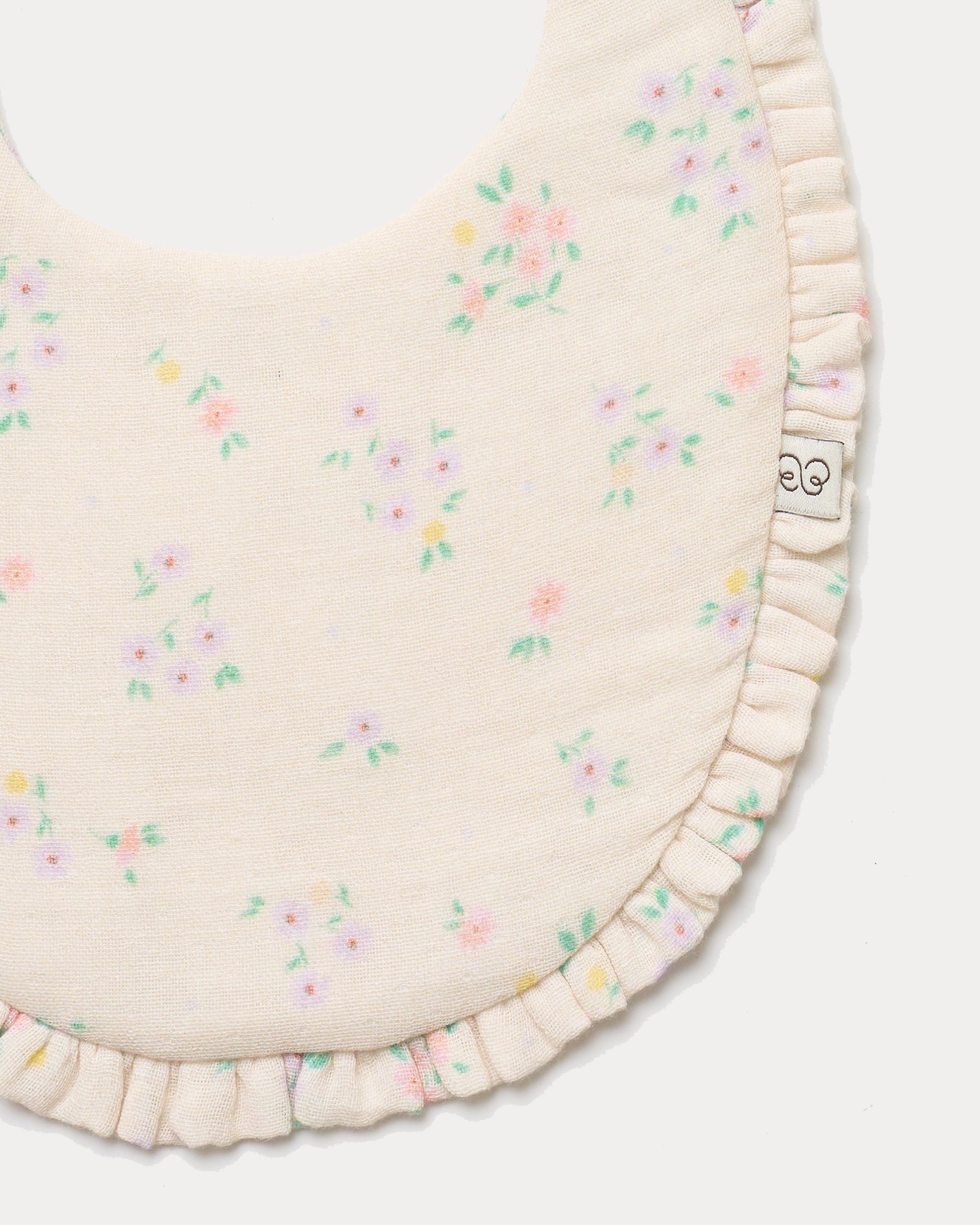 Early Sunday, Bib in Painted Bouquet print, made from Printed Cotton Double Gauze fabric, shown in a closeup flat-lay view
