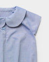 Early Sunday, Bobby Baby Romper in Summer Sky color, made from 100% Cotton Chambray fabric, featuring short sleeves with peter pan collar, shown in a closeup flat-lay view