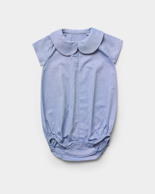 Early Sunday, Bobby Baby Romper in Summer Sky color, made from 100% Cotton Chambray fabric, featuring short sleeves with peter pan collar, shown in a front flat-lay view