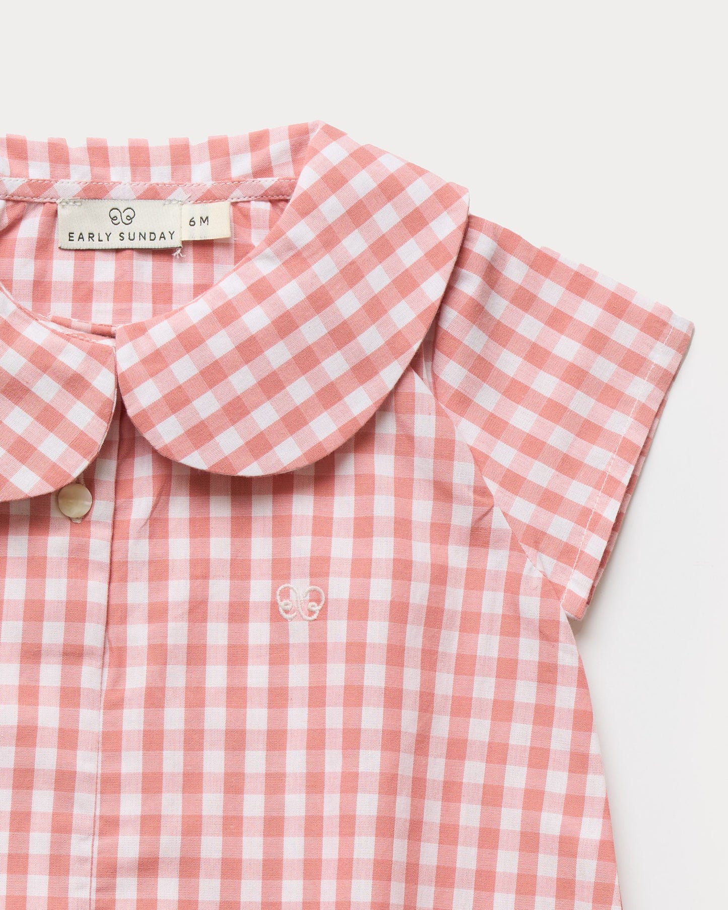 Early Sunday, Bobby Baby Romper in Peony color, made from 100% Cotton Gingham Check fabric, featuring short sleeves with peter pan collar, shown in a closeup flat-lay view