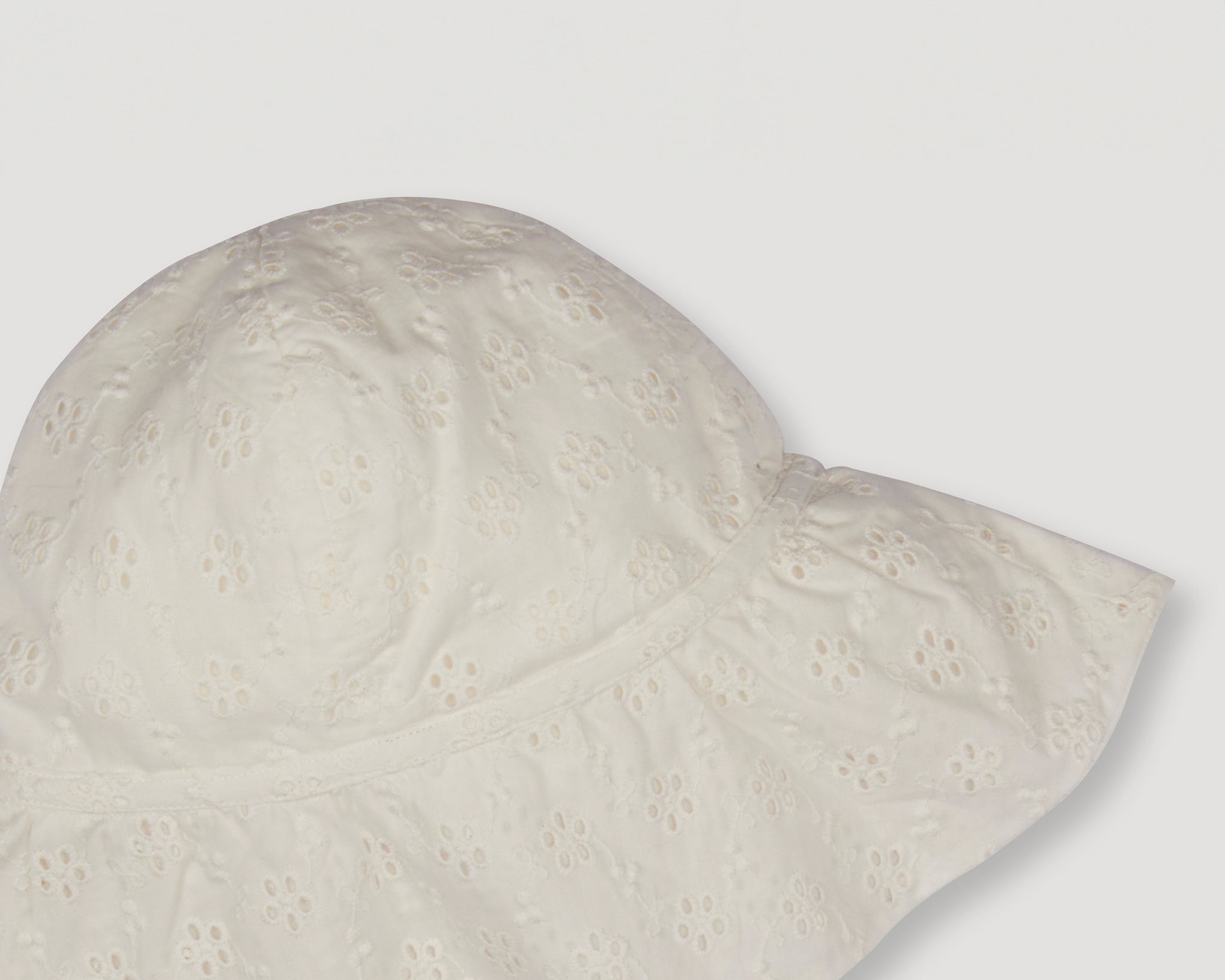 Early Sunday, Bonnie Baby Sun Hat in Ivory color, made from All-Over Eyelet Embroidered Cotton Schifflie fabric, featuring wide brim for sun protection, designed to be lightweight and comfortable for all-day wear, shown in a closeup flat-lay view