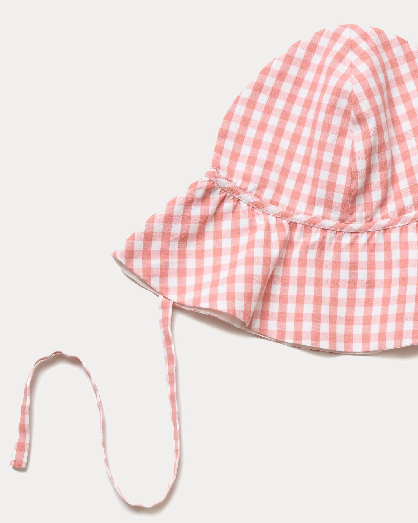 Early Sunday, Bonnie Hat Cap in Peony color, made from Gingham Check fabric, shown in a closeup flat-lay view