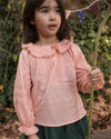 Early Sunday, Cécile Blouse in Blush, made from Cotton Swiss Dobby fabric, featuring a relaxed silhouette with gathered sleeves and delicate detailing, shown in a close up shot of model playing outdoors