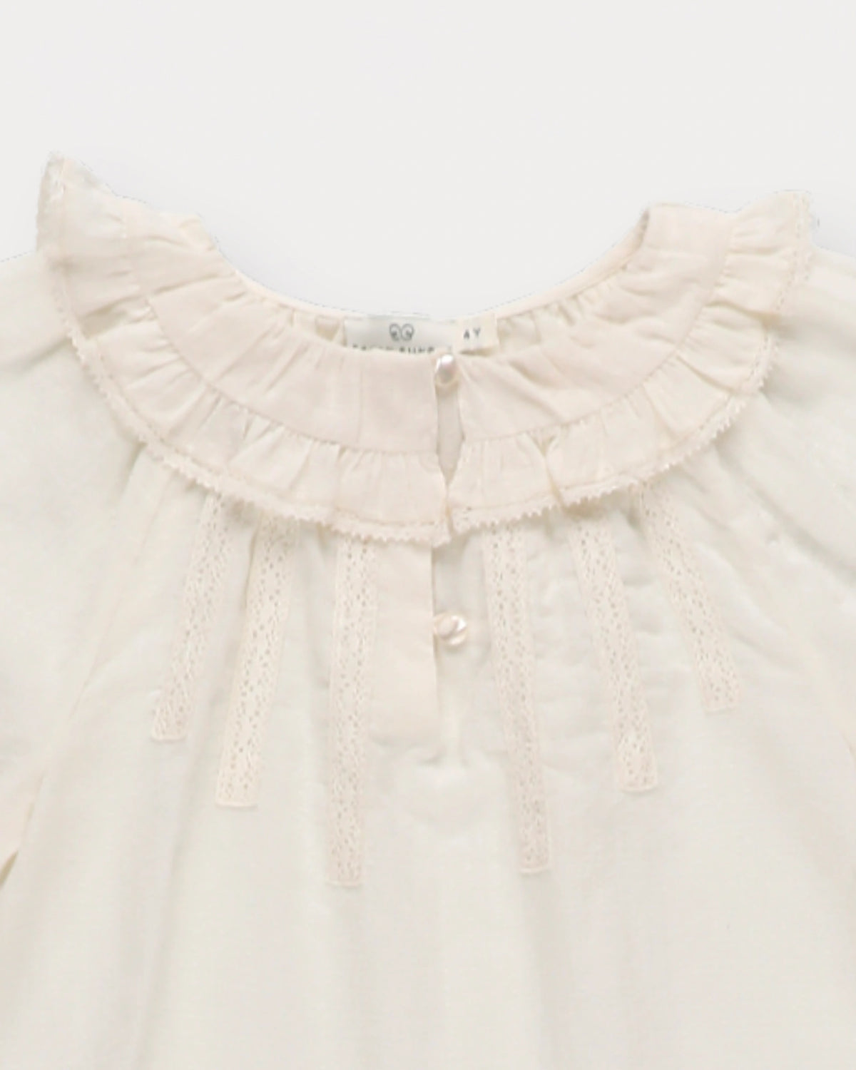 Early Sunday, Cécile Blouse in Ecru, made from Cotton Swiss Dobby fabric, featuring a relaxed silhouette with gathered sleeves and delicate detailing, shown in a closeup flat-lay view