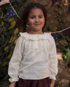 Early Sunday, Cécile Blouse in Ecru, made from Cotton Swiss Dobby fabric, featuring a relaxed silhouette with gathered sleeves and delicate detailing, shown in a front view of model wearing outdoors