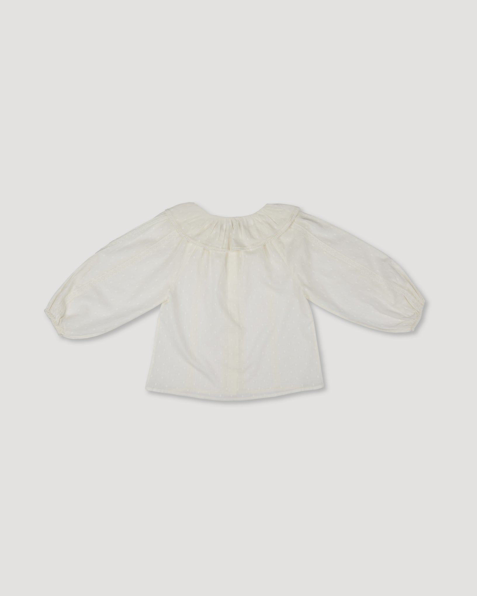 Early Sunday, Cecilia Blouse in Ecru color, made from Cotton Swiss Dobby fabric, featuring relaxed fit, frill neckline, long sleeves with elasticated cuffs, and MOP buttons, shown in a back flat-lay view