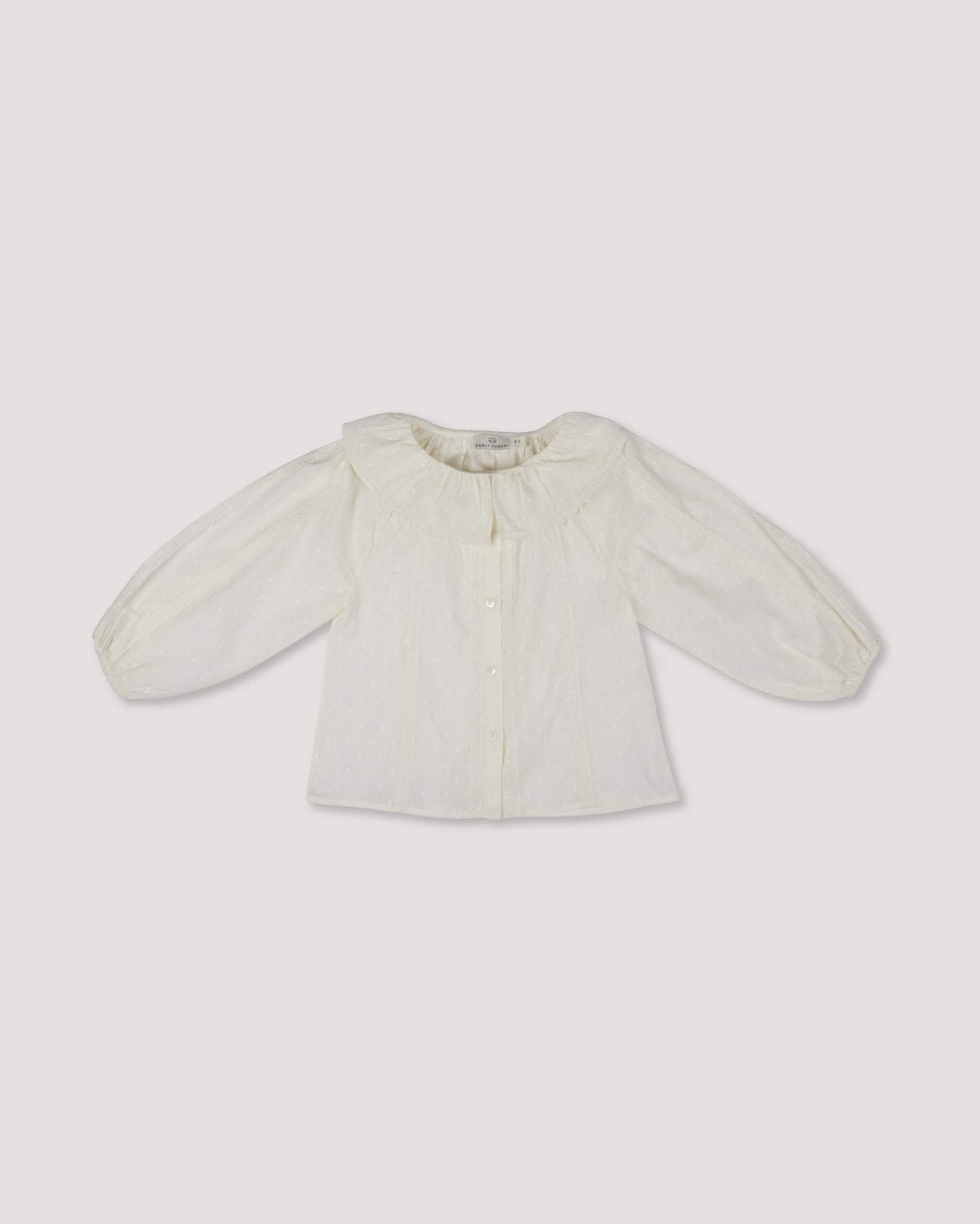 Early Sunday, Cecilia Blouse in Ecru print, made from Cotton Swiss Dobby fabric, featuring relaxed fit, frill neckline, long sleeves with elasticated cuffs, and MOP buttons, shown in a front flat-lay view