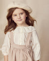 Early Sunday, Cecilia Blouse in Ecru color, made from Cotton Swiss Dobby fabric, featuring relaxed fit, frill neckline, long sleeves with elasticated cuffs, and MOP buttons, shown in an angled view of a model wearing it in a studio setting