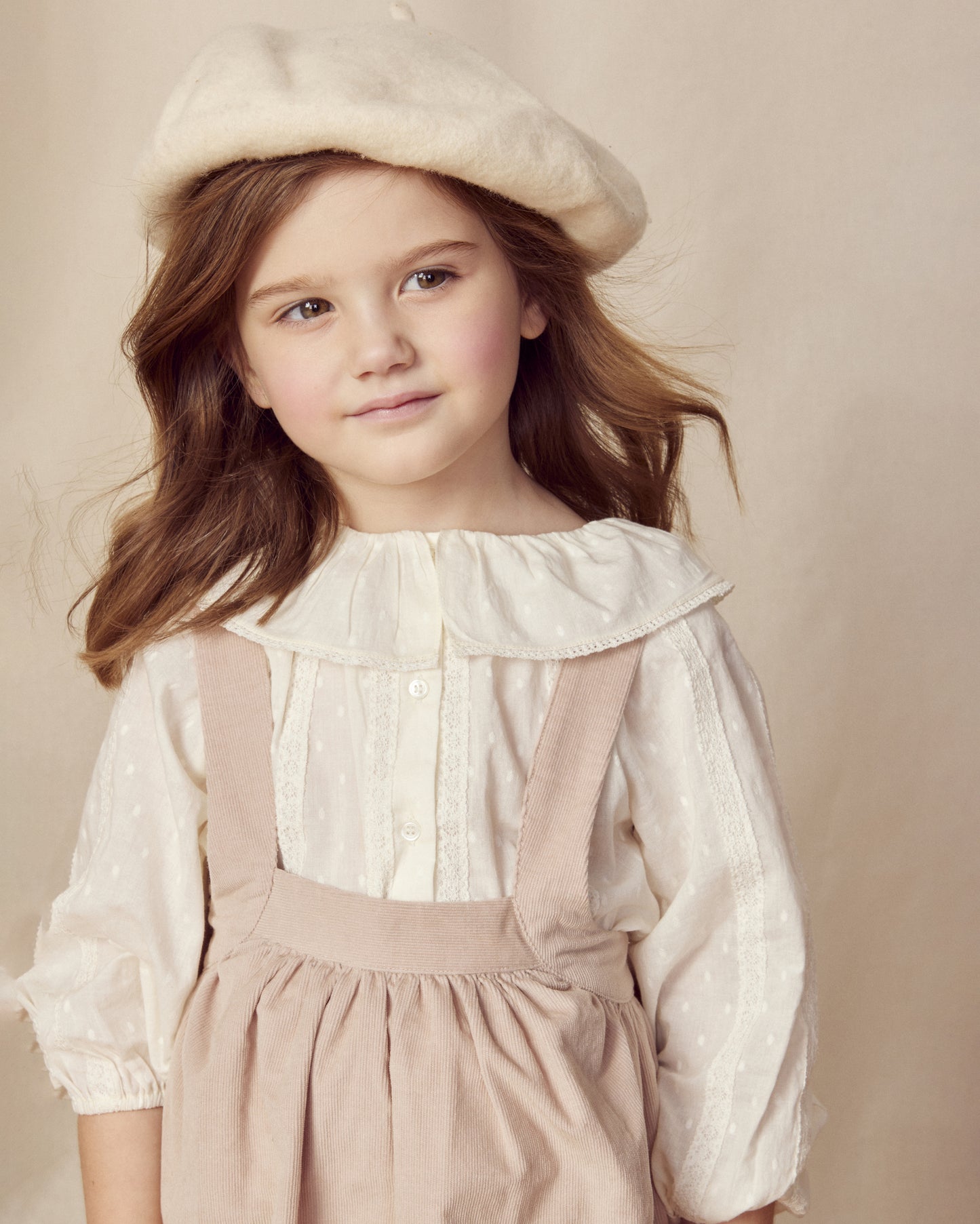 Early Sunday, Cecilia Blouse in Ecru color, made from Cotton Swiss Dobby fabric, featuring relaxed fit, frill neckline, long sleeves with elasticated cuffs, and MOP buttons, shown in an angled view of a model wearing it in a studio setting
