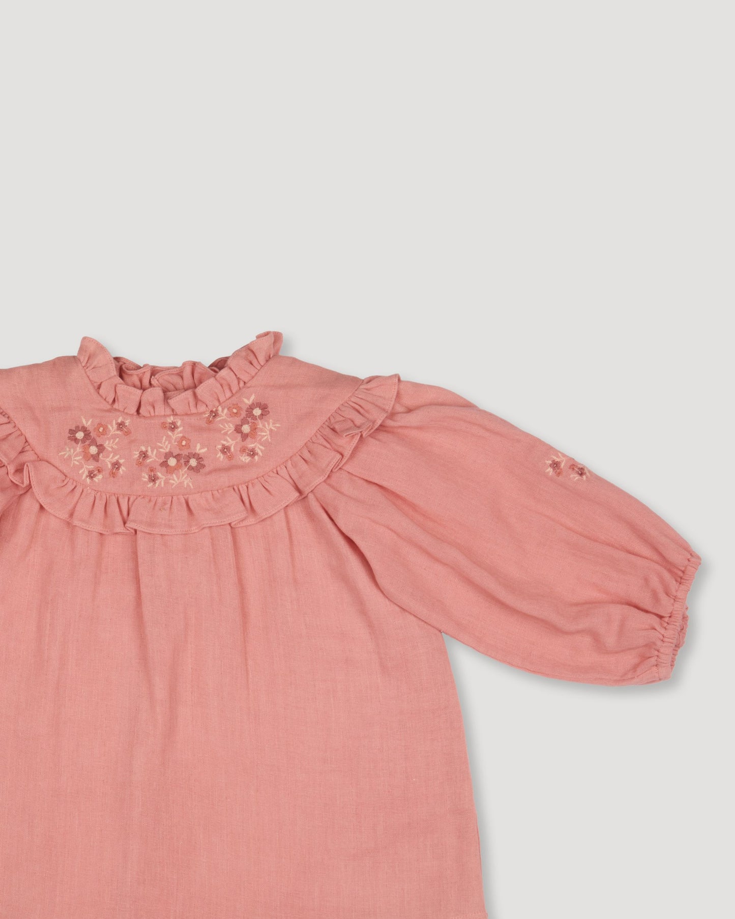 Early Sunday, Charlie Baby Dress & Bloomer Set in Rose color, made from Dyed Cotton Double Gauze fabric, featuring ruffled neckline with floral embroidery & matching bloomers, shown in a closeup flat-lay view