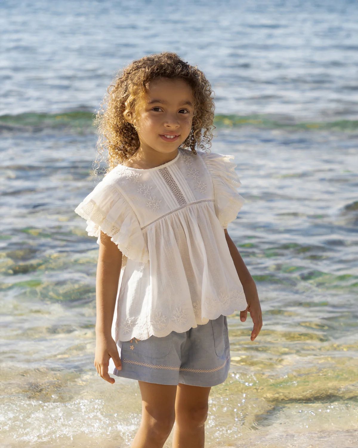 Early Sunday, Charlie Blouse in Ivory print, made from Cotton Tiny Swiss Dots fabric, featuring Flutter sleeves, pintuck detailing, and a flowy, gathered silhouette, shown in a outdoor shot of model wearing it