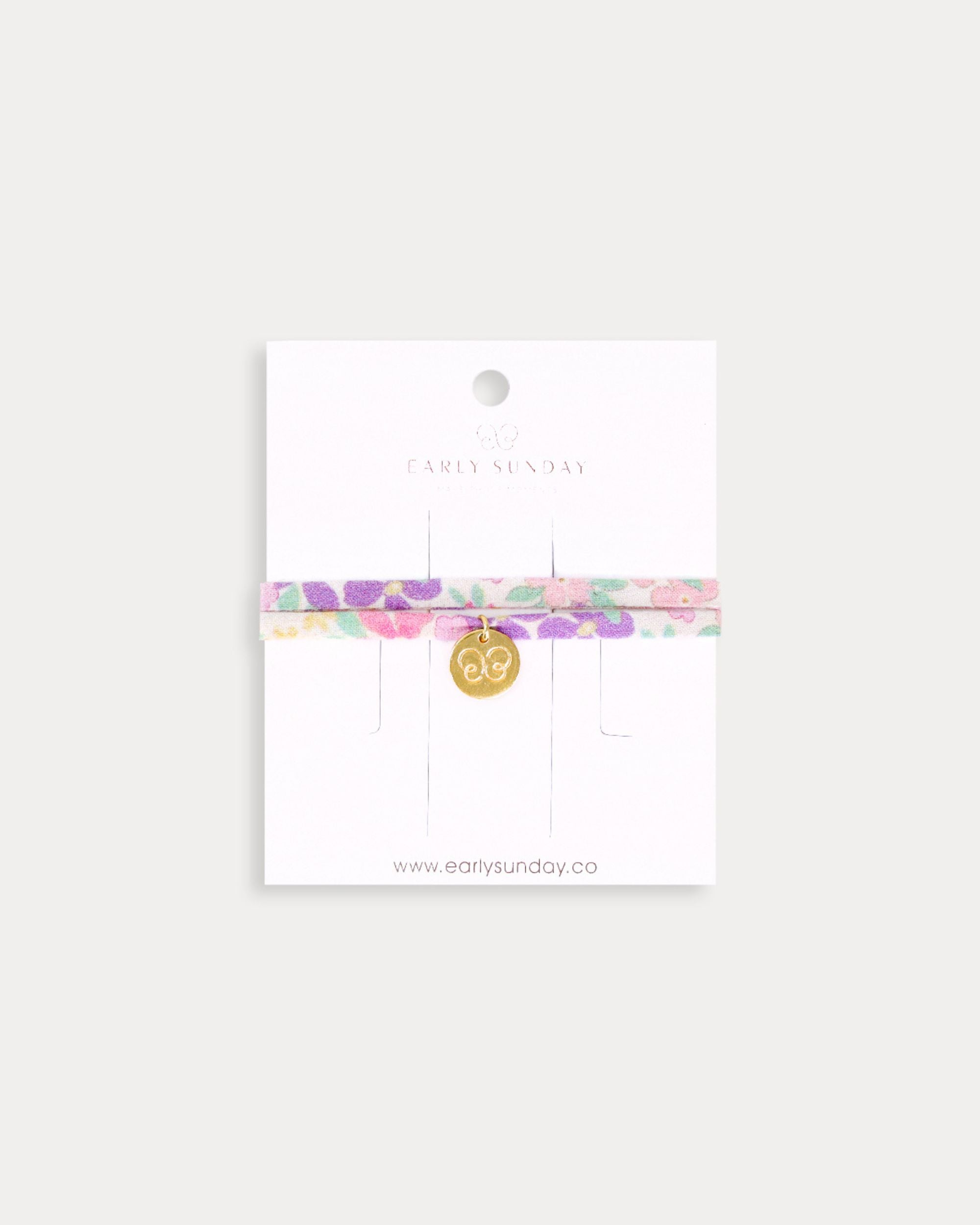 Early Sunday, Charm Bracelet in Emma Floral Purple color, made from Organic Printed Cotton Cambric fabric, featuring a soft fabric bracelet design with a charm, shown in a front flat-lay view