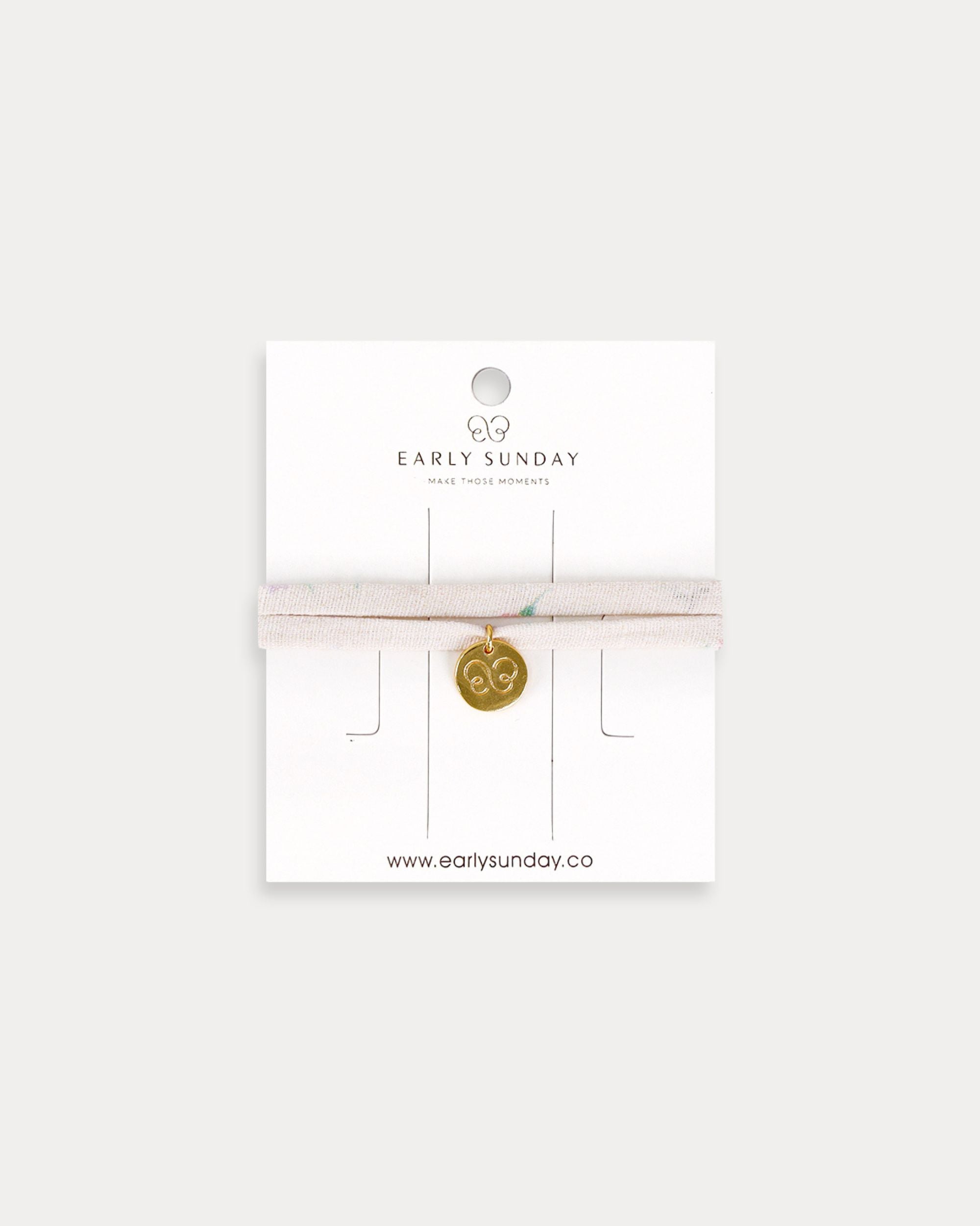 Early Sunday, Charm Bracelet in Painted Bouquet print, made from Printed 70% Cotton, 30% Linen fabric, featuring a soft fabric bracelet design with a charm, shown in a front flat-lay view