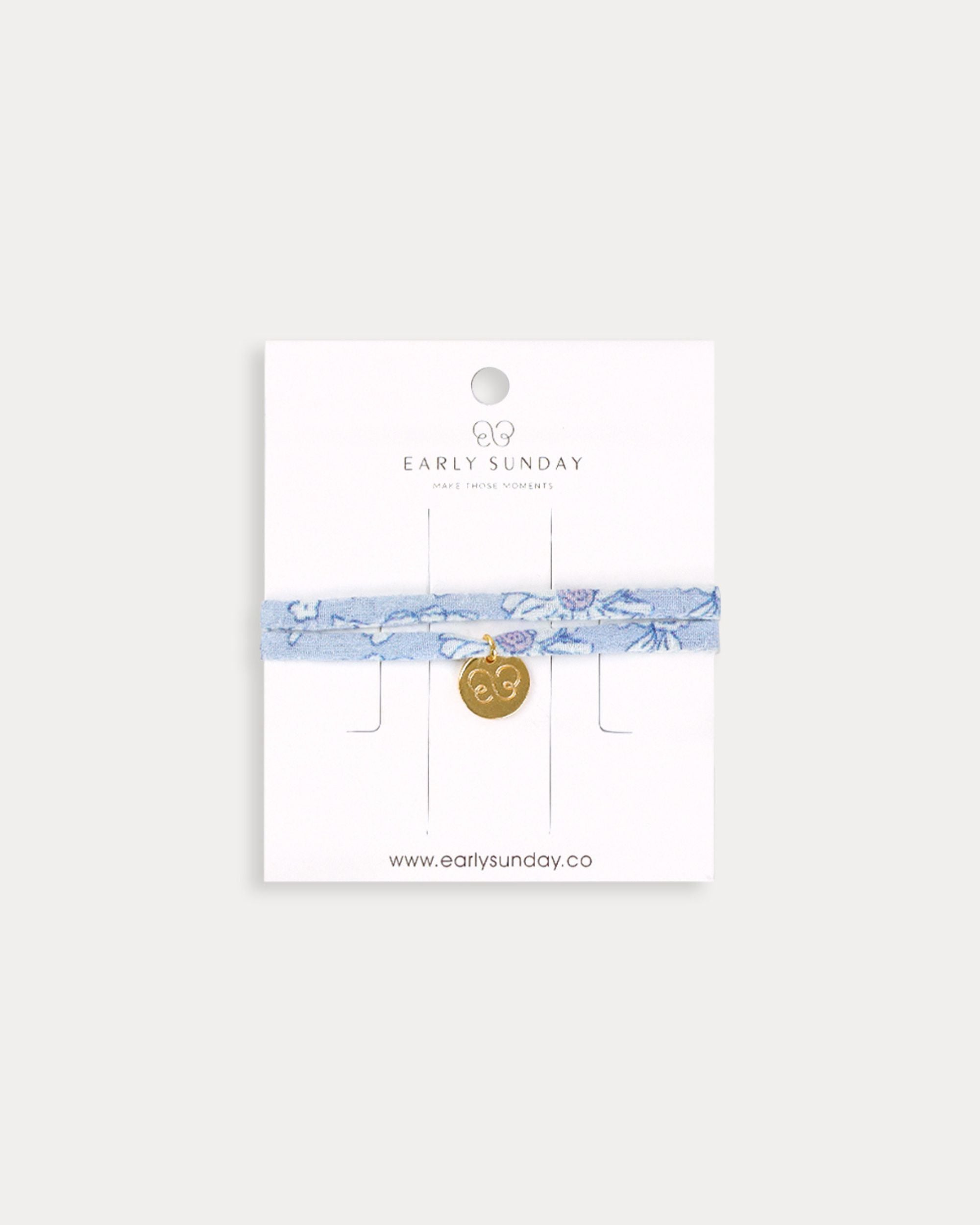 Early Sunday, Charm Bracelet in Tonal Floral Blue color, made from Printed Cotton Tiny Swiss Dobby fabric, featuring a soft fabric bracelet design with a charm, shown in a front flat-lay view