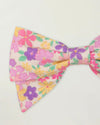 Early Sunday, Chiara Clip in Emma Floral Purple color, made from Organic Printed Cotton Cambric fabric, featuring a bow design on an alligator clip with a secure fit, shown in closeup flat-lay view