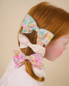 Early Sunday, Chiara Clip in Emma Floral Purple color, made from Organic Printed Cotton Cambric fabric, featuring a bow design on an alligator clip with a secure fit, shown in side view of model wearing it