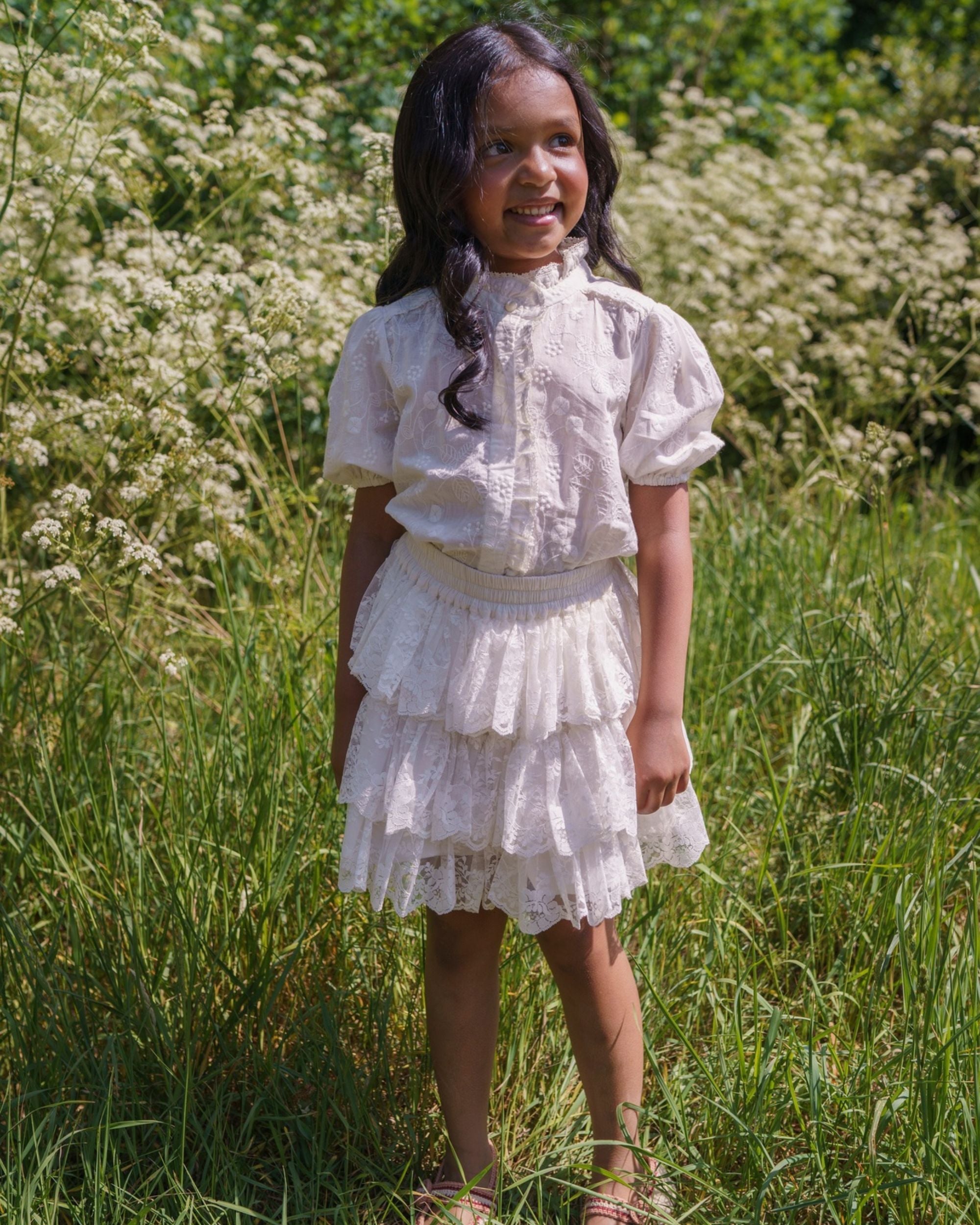 Early Sunday, Coco Blouse in Ivory color, made from all over embroidery fabric, featuring Puff sleeves, ruffled neckline and placket, shown in a model wearing outdoors